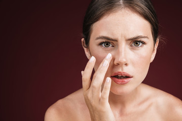 Image of displeased shirtless woman looking at camera and touching her face
