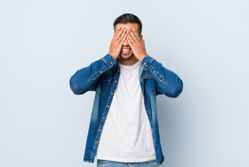 Young handsome filipino man covers eyes with hands, smiles broadly waiting for a surprise.