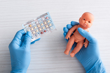 top view of doctor in latex gloves holding abortion pills and baby doll in hands