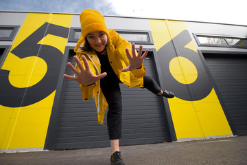 happy young caucasian woman wearing a yellow hat and a yellow raincoat dancing on a city street...