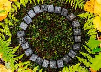 A circle of 24 Scandinavian runes on the background of moss and leaves in the autumn forest.