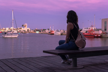 Young woman is sitting on a bench in a harbor