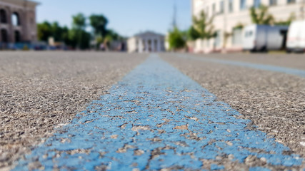 A wide blue stripe on an asphalt-black surface. asphalt road in the city, summer, green trees, blue sky. Low angle view from the middle blue lines.