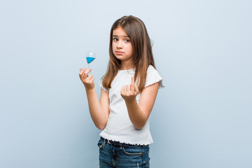 Little caucasian girl holding an hourglass pointing with finger at you as if inviting come closer.