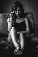 Black and white portrait of Southeast Asian woman holding gun to head while sitting on couch,...