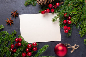 Merry Christmas card with paper, gift box, holly berries and fir tree branch on stone background....