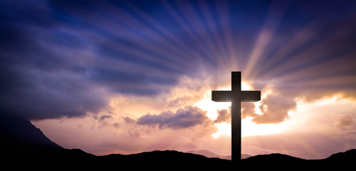 Jesus Christ cross on an amazing mountain sunset background with dramatic lighting and sunbeams....