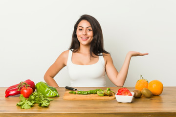 Young curvy woman preparing a healthy meal showing a copy space on a palm and holding another hand on waist.