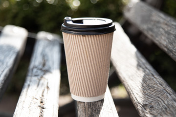 A paper coffee cup with cap on a bench