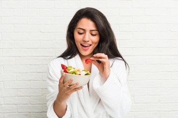 Young hispanic woman eating a fruit bowl on the bed
