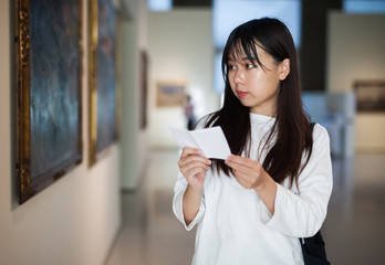 Chinese woman standing with guide-book near painting in baguette