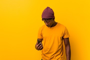 Young african man standing against a yellow background wearing a hat and using a phone