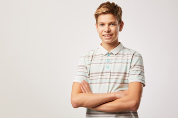 Portrait of boy with blond hair in casual T-shirt standing with arms crossed and smiling at camera over white background