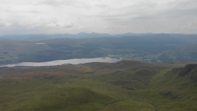 An aerial backward footage of a grassy mountain plateau with a huge lake and mountain range in the background under a cloudy sky	