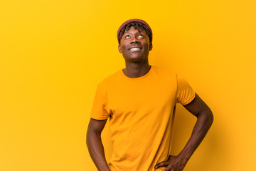 Young black man wearing rastas over yellow background confused, feels doubtful and unsure.