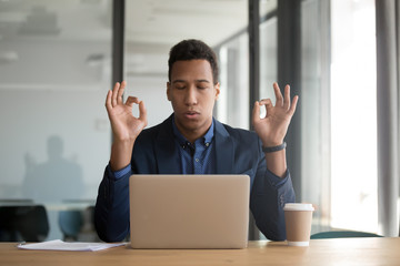 Calm mindful black businessman in suit meditate at work desk