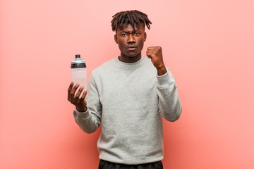 Young fitness black man holding a water bottle showing fist to camera, aggressive facial expression.