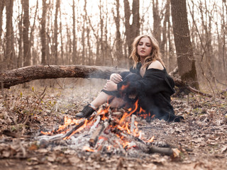 Young woman sitting near the bonfire in forest.