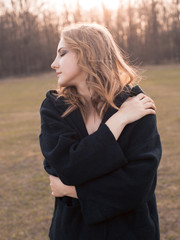 A young woman in black clothes posing outdoors at sunset