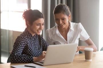 Smiling diverse female coworkers discuss online work using laptop