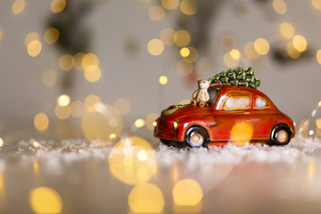 Decorative figurines of a Christmas theme. A statuette of a red car on which a teddy bear sits. Christmas tree decoration. Festive decor, warm bokeh lights.