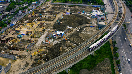 Aerial view of urban construction site next to elevated train line and busy city road, showcasing...