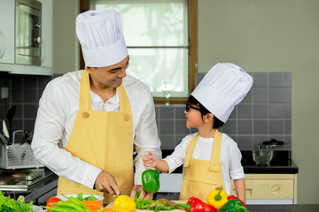 Happy Asian father  and son  in chef hats preparing  healthy food in kitchen at home , family healthy lifestyle concept