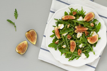 Salad with arugula, figs, cheese, walnut and honey. Autumn salad with figs and cheese on a white plate.