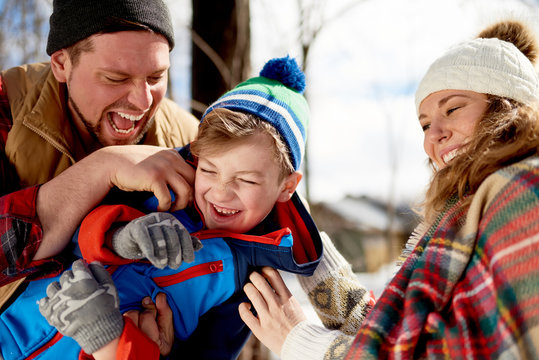 Mother and father enjoying playing in fresh snow during wintertime and tickling their son while laughing