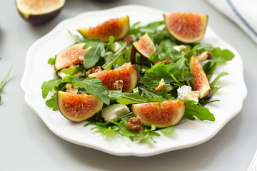 Salad with arugula, figs, cheese, walnut and honey. Autumn salad with figs and cheese on a white plate.