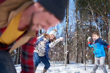 Happy family with son enjoying playing in fresh snow during wintertime and having a snowball fight