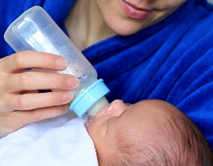 baby in mother's arms and wrapped up in white blanket just been fed a bottle of milk after having a good sleep in bed stock photograph stock photo