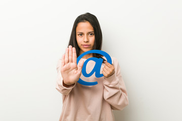 Young hispanic woman holding an at icon standing with outstretched hand showing stop sign, preventing you.