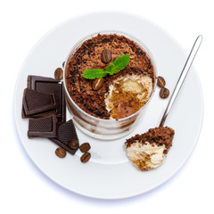 Classic tiramisu dessert in a glass cup on the plate and pieces of chocolate on white background with clipping path