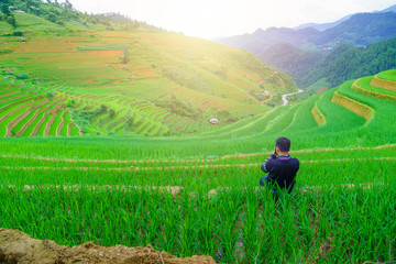 Fototapeta na wymiar Young men sitting and taking pictures beautiful terraced rice paddy field and mountain landscape in Mu Cang Chai and SAPA VIETNAM Sunlight and flare background concept.