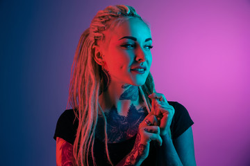 Caucasian young woman's portrait on gradient background in neon light. Beautiful female model with unusual look. Concept of human emotions, facial expression, sales, ad. Looking ar side, smiles. - obrazy, fototapety, plakaty