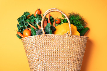 Straw basket with organic vegetables over trendy yellow background. Healthy food, vegetarian diet....