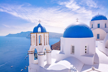 Beautiful Oia town on Santorini island, Greece. Traditional white architecture  and greek orthodox churches with blue domes over the Caldera, Aegean sea. Scenic travel background. - obrazy, fototapety, plakaty