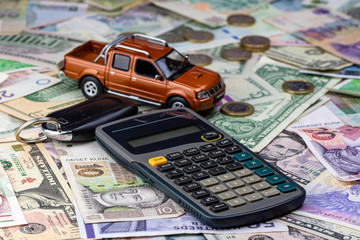 Calculator, keys and pickup toy car on a variety of national currency banknotes background.  Concept of the cost of purchasing, renting and maintaining a car.