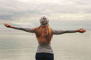 A beautiful girl stands on the shore with her back to the camera. Hands up. Sunset. Yoga classes.