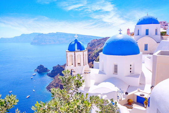 Beautiful Oia town on Santorini island, Greece. Traditional white architecture and greek orthodox churches with blue domes over the Caldera, Aegean sea. Scenic travel background. © MarinadeArt