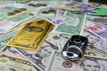 A car key on the background of various currency notes and one symbolic gold dollar banknote. Concept of the cost of purchasing, renting and maintaining a car.
