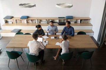 Multicultural business team listening to male boss at group meeting