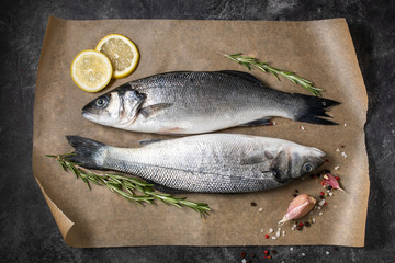 Fresh fish seabass and ingredients for cooking, lemon and rosemary. Dark background top view.