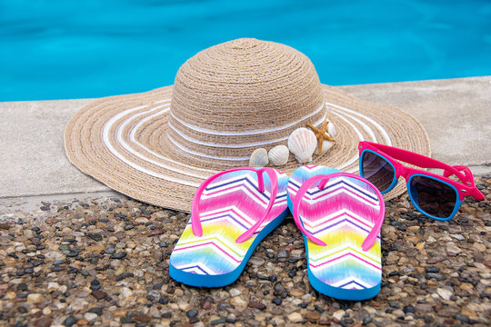 summer hat and flip-flops with sunglasses by swimming pool