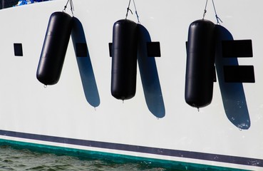 View on white boat side of luxury yacht with three black fenders in natural bright sun light -...