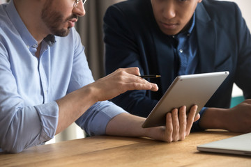 Diverse businessmen talking using digital tablet sit at desk, closeup