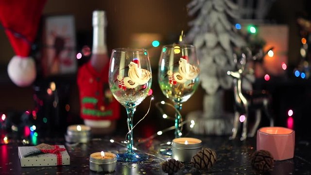 The shower of gold sequins fall into a couple of decorated festive wineglasses.Glasses are surrounded with objects symbolizing Christmas and New Year celebration. Cosy home atmosphere is on the shot