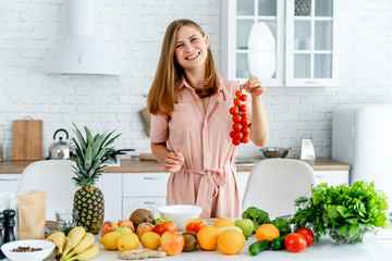 Woman in kitchen ready to prepare meal with vegetables and fruits. Woman is holding tomatoes. Kitchen background. Healthy food. Vegans. Vegeterian. Banch of tomatoes.