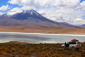 Off road in the Bolivia desert. 4x4 vehicles crossing the beautiful landscapes of the highlands. Mountain in the background and a beautiful lake with calm waters